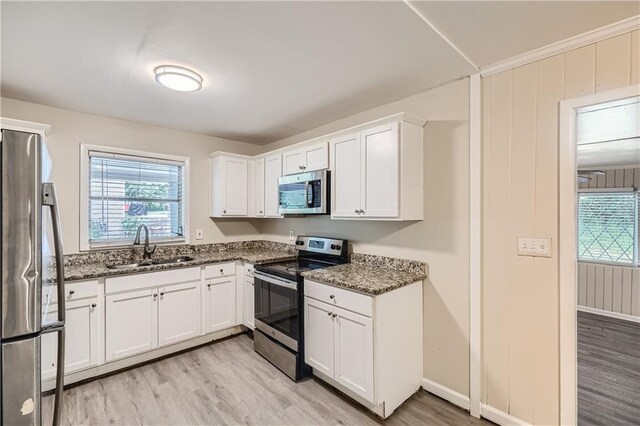 kitchen featuring appliances with stainless steel finishes, white cabinets, light hardwood / wood-style flooring, dark stone counters, and sink