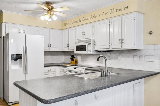 kitchen with white appliances, dark countertops, a peninsula, and a sink