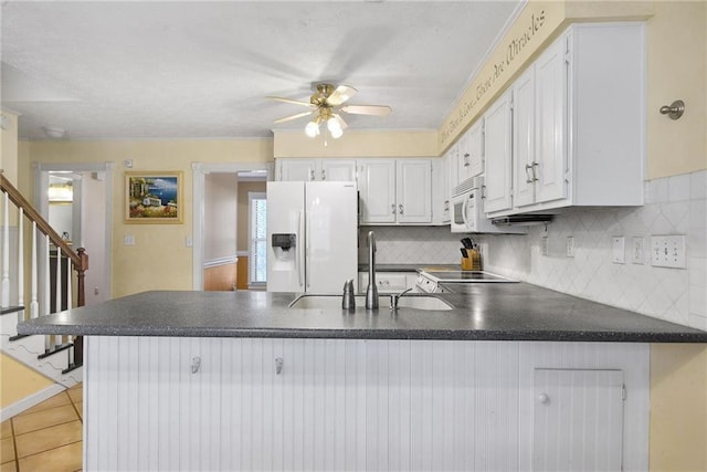 kitchen featuring white appliances, white cabinets, dark countertops, and a peninsula