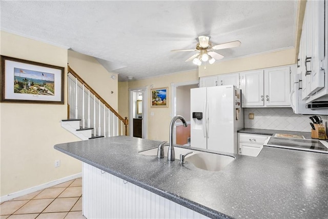 kitchen featuring a sink, dark countertops, white cabinetry, white fridge with ice dispenser, and a peninsula