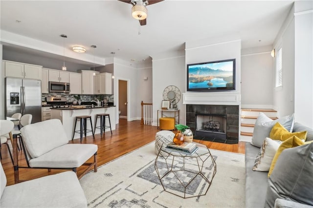 living room with ceiling fan, sink, light wood-type flooring, and a fireplace