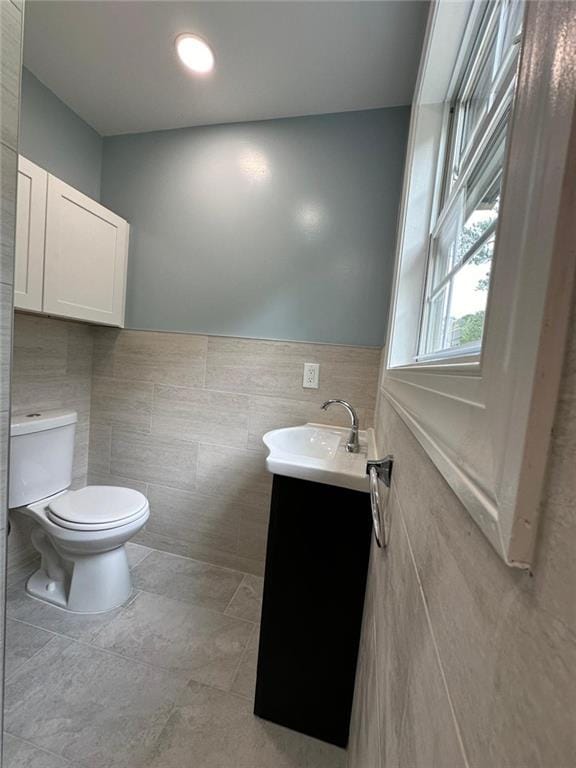 half bathroom featuring tile patterned flooring, a wainscoted wall, toilet, vanity, and tile walls