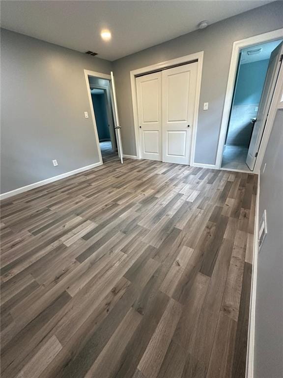unfurnished bedroom featuring a closet, wood finished floors, visible vents, and baseboards