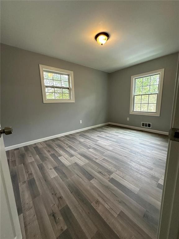 spare room with plenty of natural light, baseboards, visible vents, and dark wood finished floors