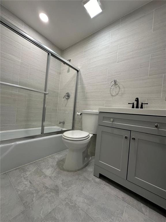 bathroom featuring tile walls, vanity, enclosed tub / shower combo, and toilet