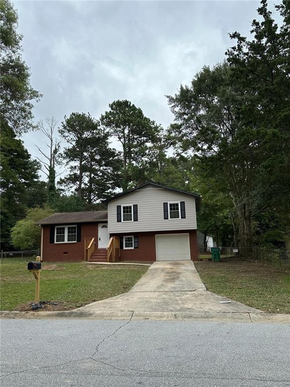 tri-level home featuring an attached garage, a front lawn, concrete driveway, and fence