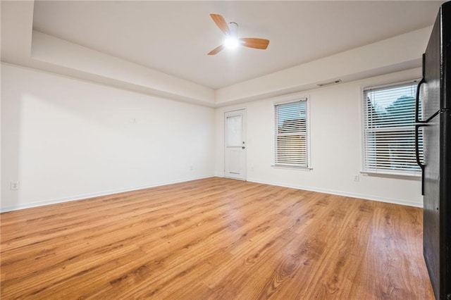 unfurnished room with light wood-type flooring, ceiling fan, and a raised ceiling