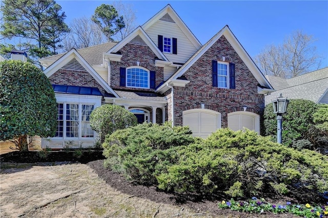 view of front of property featuring a garage, brick siding, and roof with shingles