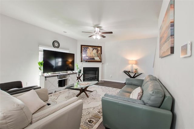 living area featuring ceiling fan, baseboards, wood finished floors, and a glass covered fireplace