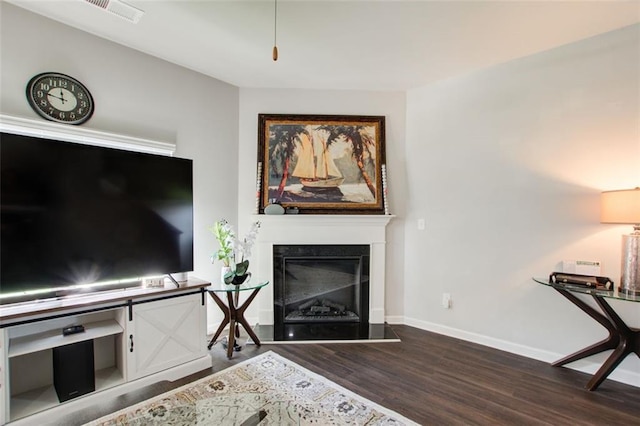 living area with a fireplace with raised hearth, wood finished floors, visible vents, and baseboards