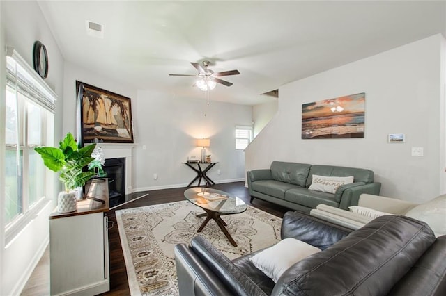 living area with a fireplace with raised hearth, dark wood-style flooring, visible vents, and baseboards