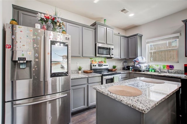 kitchen with light stone counters, gray cabinets, visible vents, appliances with stainless steel finishes, and a kitchen island