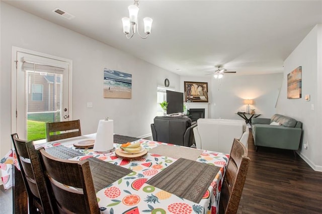 dining area with baseboards, visible vents, a glass covered fireplace, wood finished floors, and ceiling fan with notable chandelier