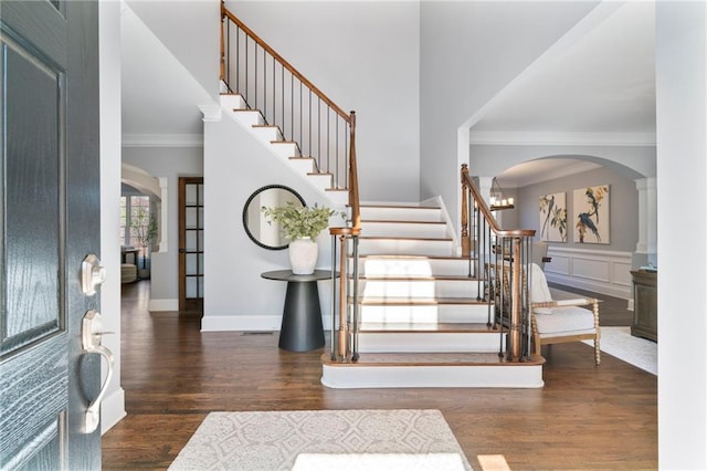 foyer featuring arched walkways, a decorative wall, stairway, ornamental molding, and wood finished floors