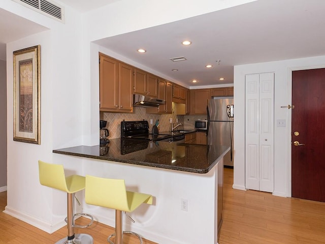 kitchen with stainless steel appliances, kitchen peninsula, dark stone counters, and a kitchen bar