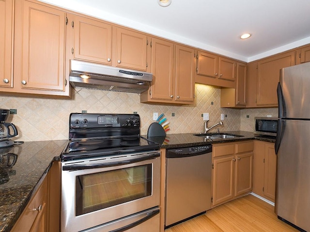 kitchen with sink, dark stone countertops, backsplash, stainless steel appliances, and light hardwood / wood-style floors