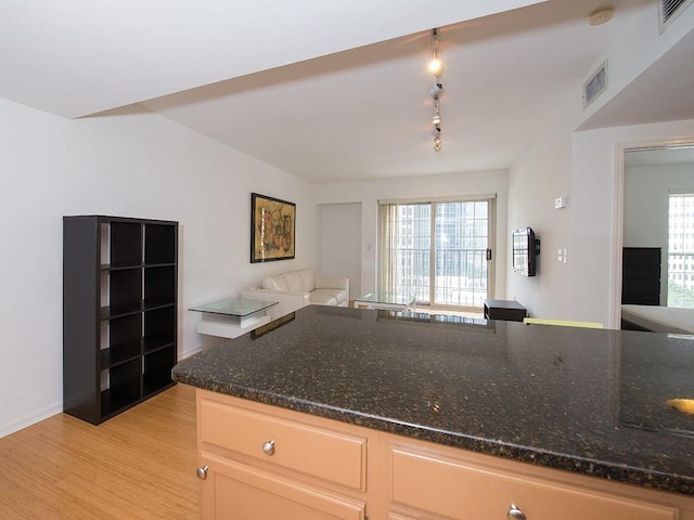 kitchen with rail lighting, dark stone counters, light brown cabinetry, and light hardwood / wood-style flooring