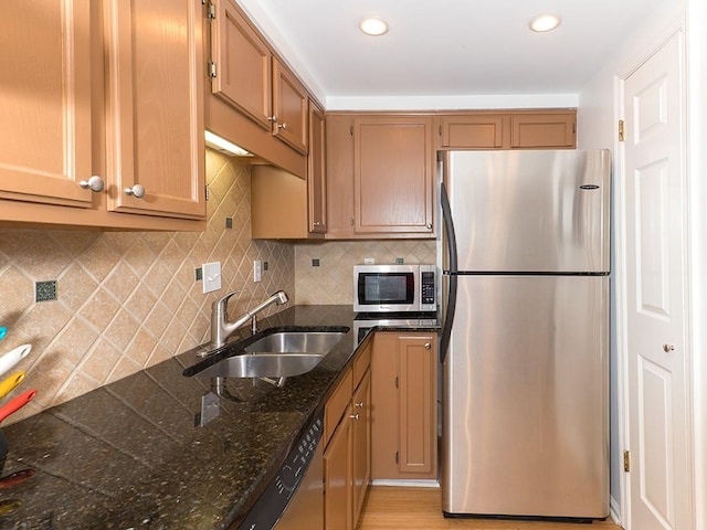 kitchen with stainless steel appliances, sink, backsplash, and dark stone counters