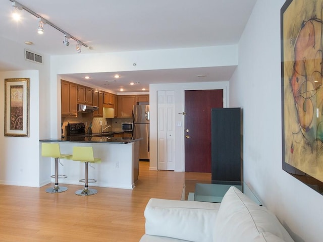 kitchen featuring stainless steel appliances, tasteful backsplash, a kitchen bar, kitchen peninsula, and light wood-type flooring