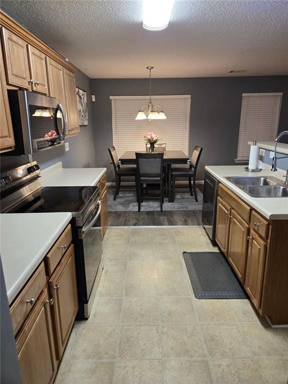 kitchen featuring sink, appliances with stainless steel finishes, an inviting chandelier, hanging light fixtures, and a textured ceiling