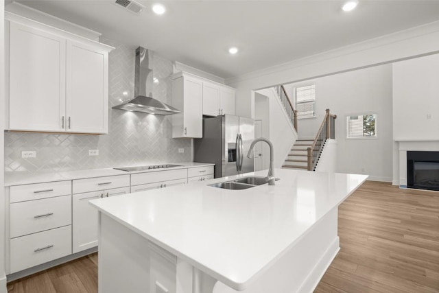 kitchen featuring white cabinetry, wall chimney exhaust hood, and a kitchen island with sink