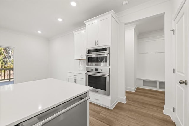 kitchen with stainless steel double oven, crown molding, light hardwood / wood-style flooring, and white cabinets