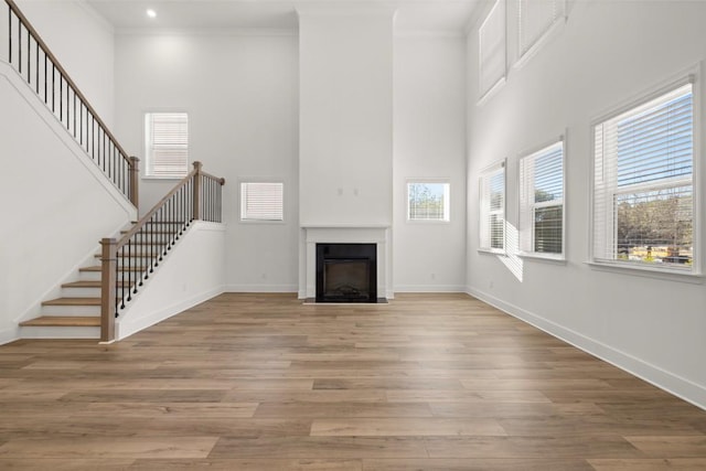 unfurnished living room with crown molding, a towering ceiling, and light hardwood / wood-style flooring