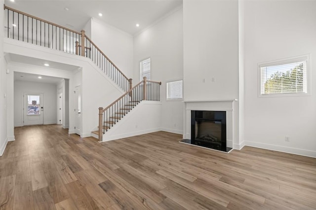 unfurnished living room with crown molding, a towering ceiling, and light hardwood / wood-style flooring