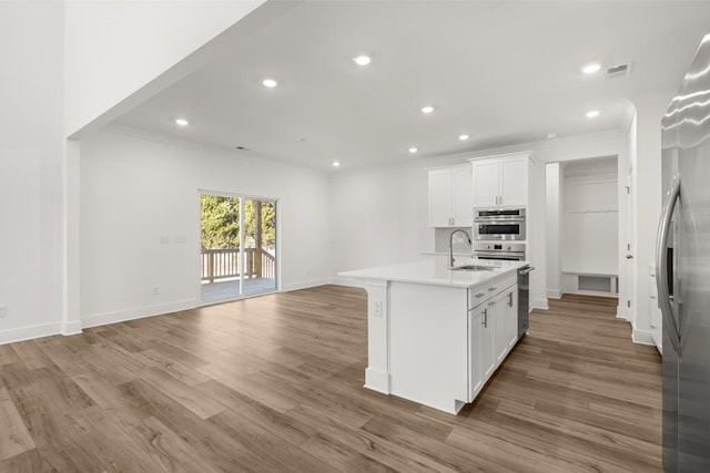 kitchen with sink, white cabinetry, wood-type flooring, stainless steel fridge, and a kitchen island with sink