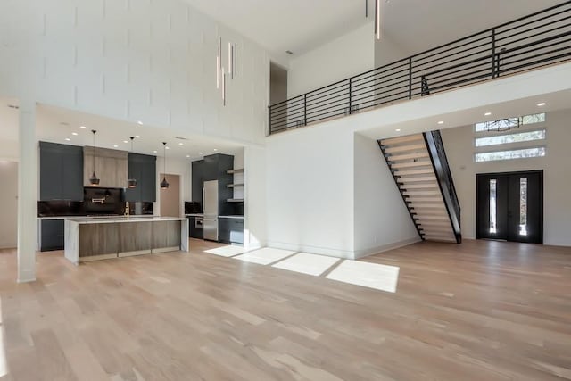 unfurnished living room featuring a towering ceiling, french doors, and light wood-type flooring