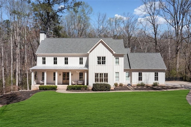 view of front facade with roof with shingles, a porch, a chimney, board and batten siding, and a front yard