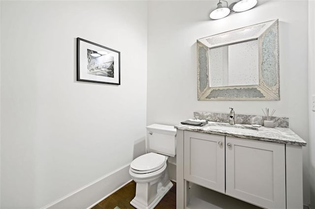 half bathroom featuring toilet, vanity, wood finished floors, and baseboards