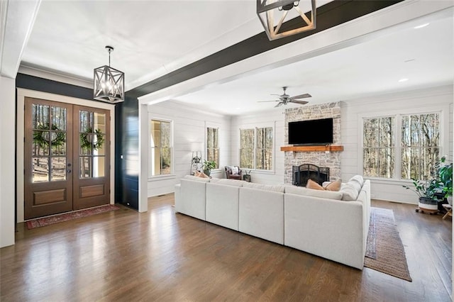 living room featuring french doors, dark wood-style flooring, recessed lighting, ceiling fan with notable chandelier, and a stone fireplace