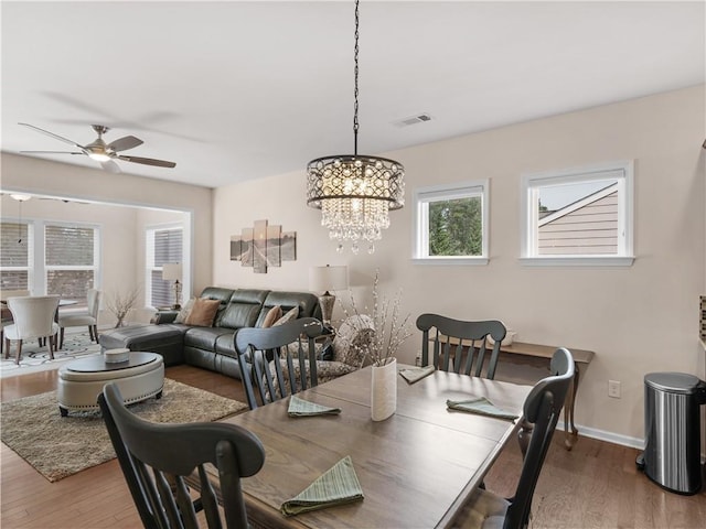 dining space with visible vents, baseboards, wood finished floors, and ceiling fan with notable chandelier