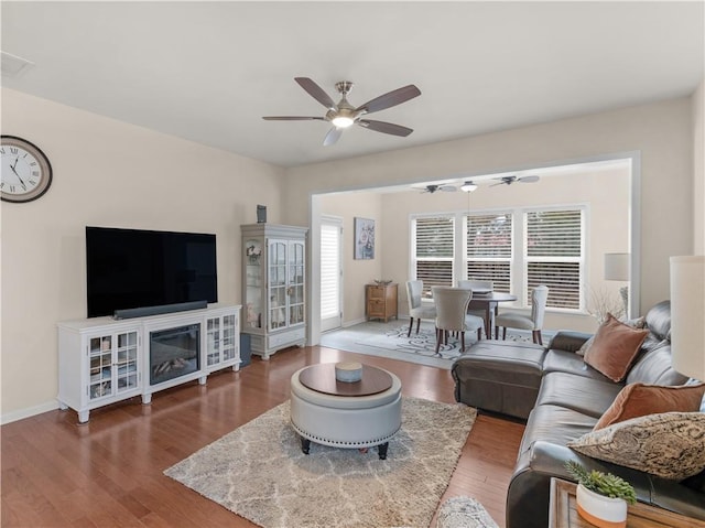 living room with a ceiling fan, visible vents, wood finished floors, and baseboards