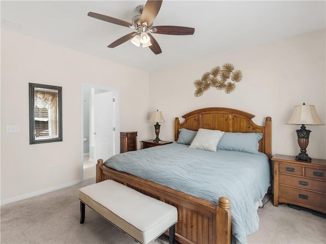 bedroom featuring baseboards, light colored carpet, ensuite bath, and a ceiling fan