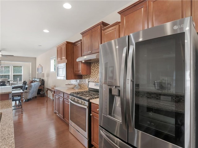 kitchen with tasteful backsplash, under cabinet range hood, open floor plan, appliances with stainless steel finishes, and wood finished floors