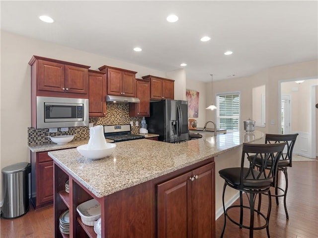 kitchen featuring under cabinet range hood, stainless steel appliances, backsplash, and wood finished floors