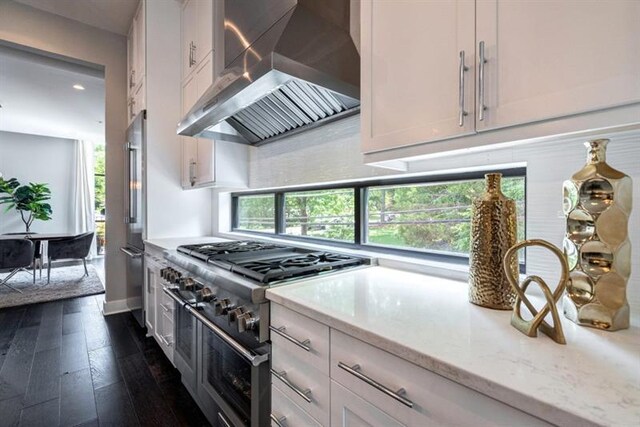 kitchen with dark hardwood / wood-style floors, double oven range, light stone countertops, wall chimney exhaust hood, and white cabinetry