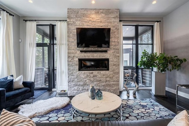 living room featuring a stone fireplace and dark wood-type flooring