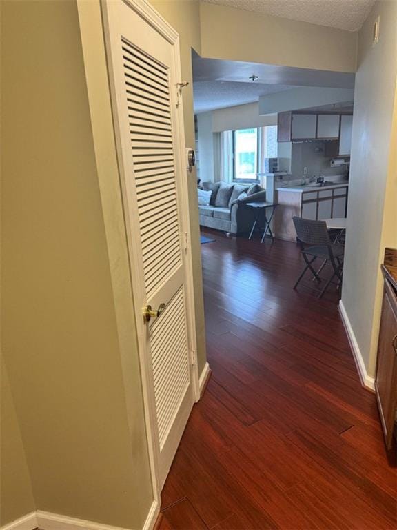 hall featuring a textured ceiling, dark wood-type flooring, and baseboards