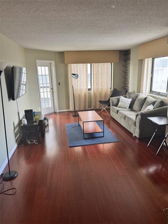 living area with a wealth of natural light, dark wood-style flooring, a textured ceiling, and baseboards