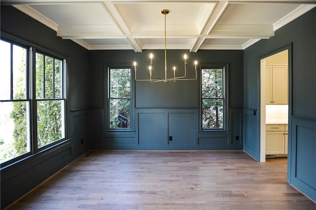 unfurnished dining area with coffered ceiling, beam ceiling, light hardwood / wood-style floors, and an inviting chandelier