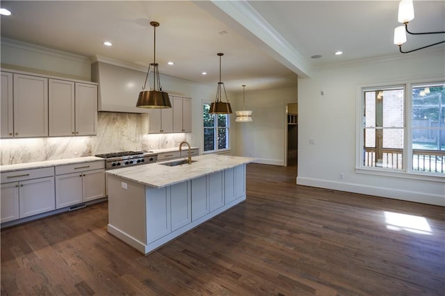 kitchen featuring sink, tasteful backsplash, light stone counters, pendant lighting, and a kitchen island with sink