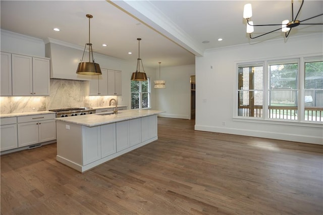 kitchen featuring tasteful backsplash, a kitchen island with sink, white cabinets, and decorative light fixtures