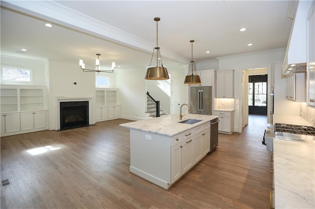 kitchen featuring white cabinetry, appliances with stainless steel finishes, light stone countertops, and a kitchen island with sink