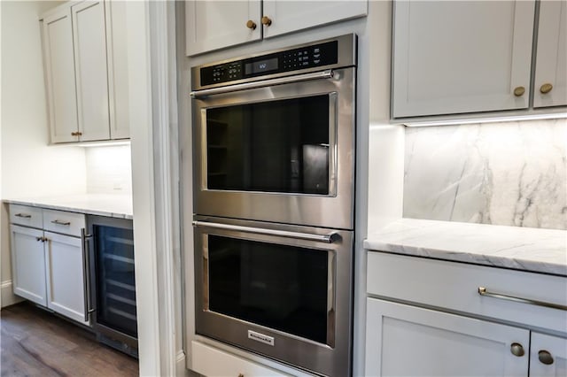 kitchen with light stone countertops, dark wood-type flooring, beverage cooler, and double oven