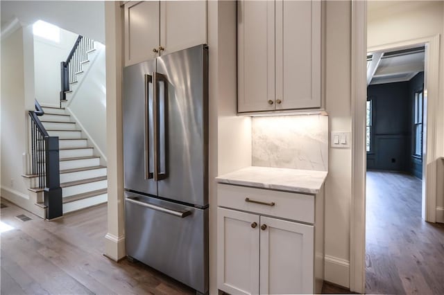 kitchen featuring backsplash, high end refrigerator, light stone counters, and light wood-type flooring