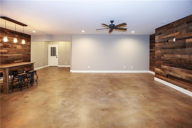 unfurnished living room featuring ceiling fan and wooden walls