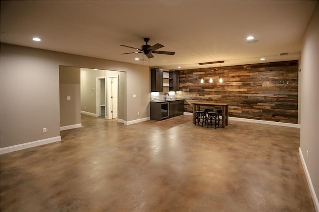 interior space featuring ceiling fan, beverage cooler, sink, and wood walls